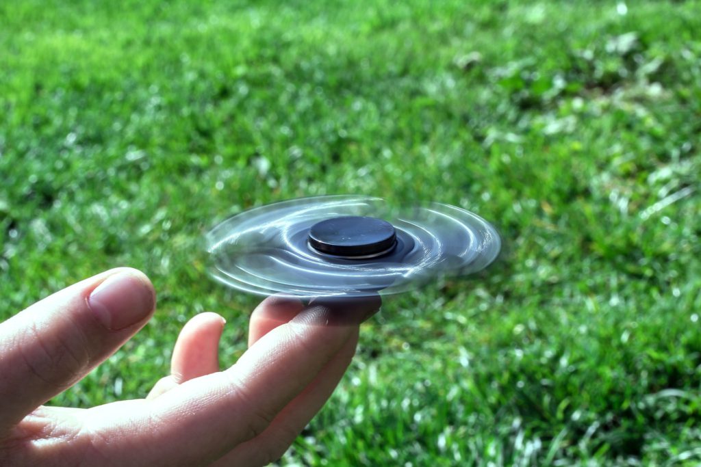 En fidget spinner snurrar på ett finger mot bakgrund av grönt gräs.