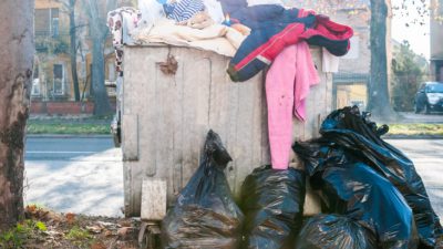 En stor container med sopor. Ur containern hänger det slängda kläder.
