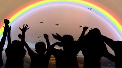 Barns silhuetter står och hejar på en regnbåge