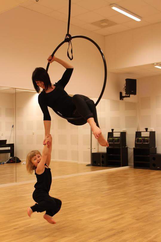 En kvinna sitter i en ring som hänger från taket och håller ett barn i handen.