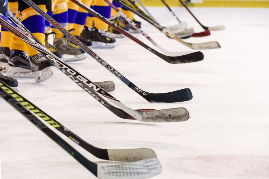 Bild på ett hockeylag som tackar motståndarna efter en match. De står med sina hockeklubbor lutade mot isen.
